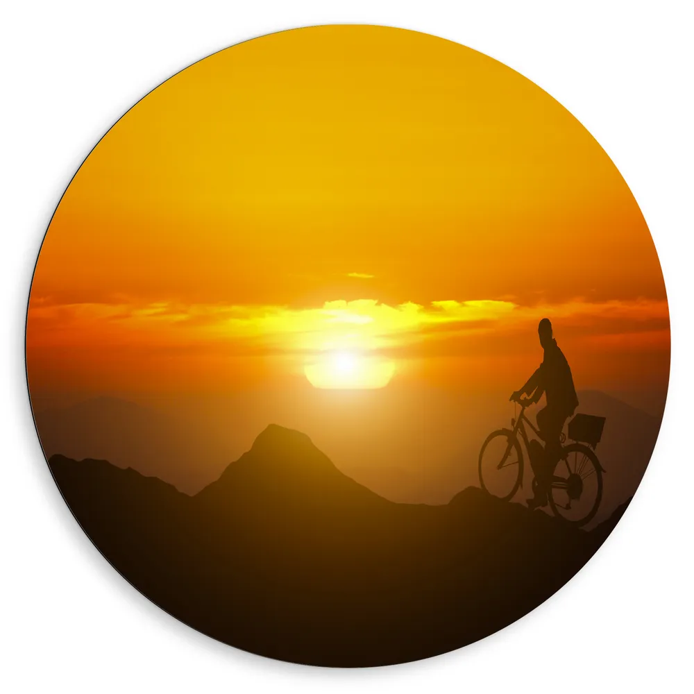 Dibond Muurcirkel - Silhouet van Man Fietsend over Kronkelende Bergtoppen bij Felkleurige Zonsondergang