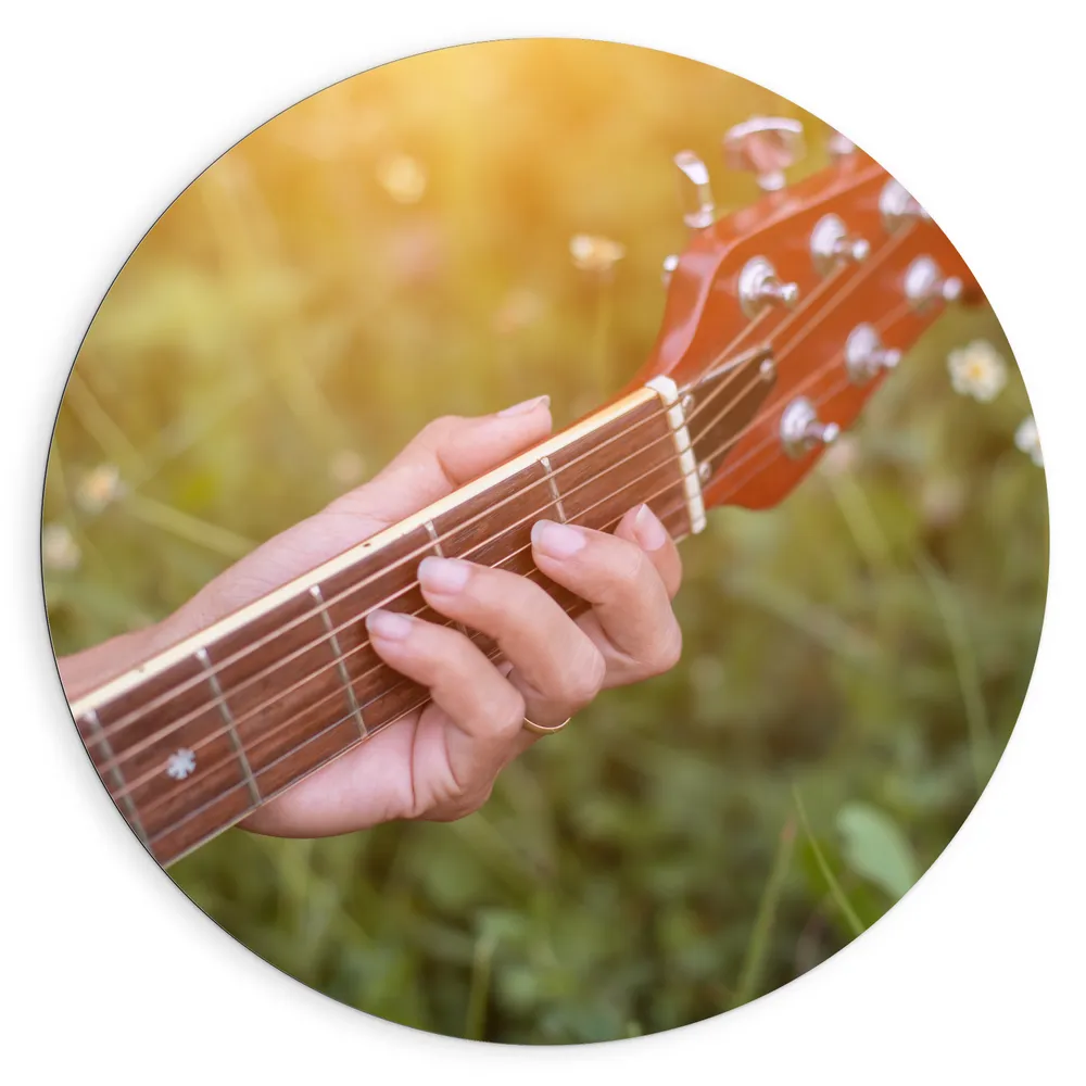 Dibond Muurcirkel - Close-up van Vrouwenhand op Bruine Gitaar in Bloemenveld