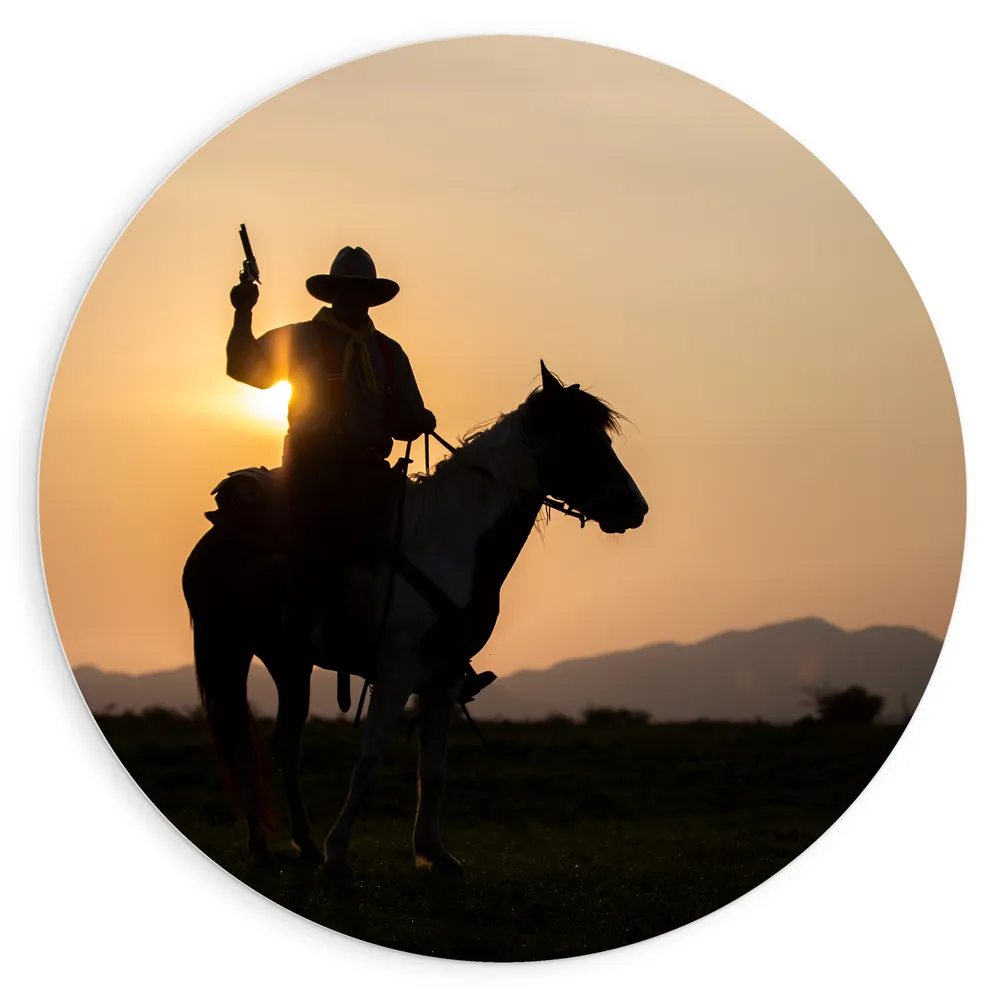 Dibond Muurcirkel - Zonsondergang achter Cowboy op Bruin met Wit Paard met Geweer